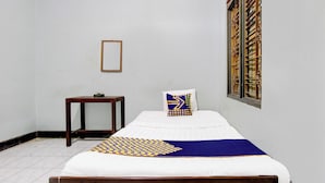 Una cama individual con edredón estampado, una mesita de noche pequeña y una ventana con barandillas decorativas.