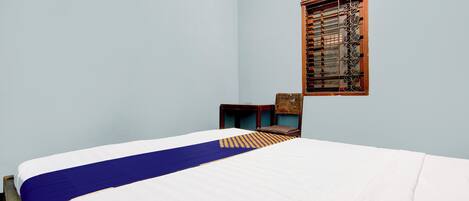 A bedroom with a bed, a window with a metal grill, and a chair.