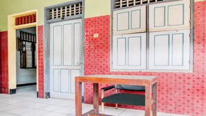 Una habitación con piso de baldosas, una mesa de madera con un asiento negro y una puerta con reja metálica.