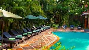 A poolside area with sun loungers and umbrellas, surrounded by lush greenery. - YASODHARAPURA RESIDENCE (Siem Reap)