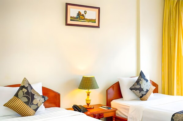 A hotel room with two beds, a nightstand with a lamp, a phone, and a framed picture on the wall. - YASODHARAPURA RESIDENCE (Siem Reap)