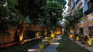 A well-maintained garden pathway with a wooden fence and plants on either side, leading to a building with a tiled roof. - YASODHARAPURA RESIDENCE (Siem Reap)