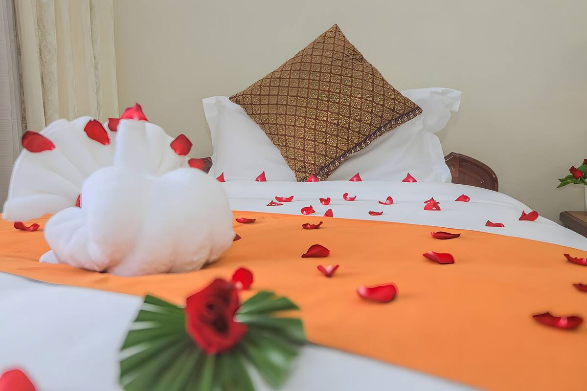 A neatly made bed with a white and orange bedspread, a decorative white swan pillow, and a patterned pillow.