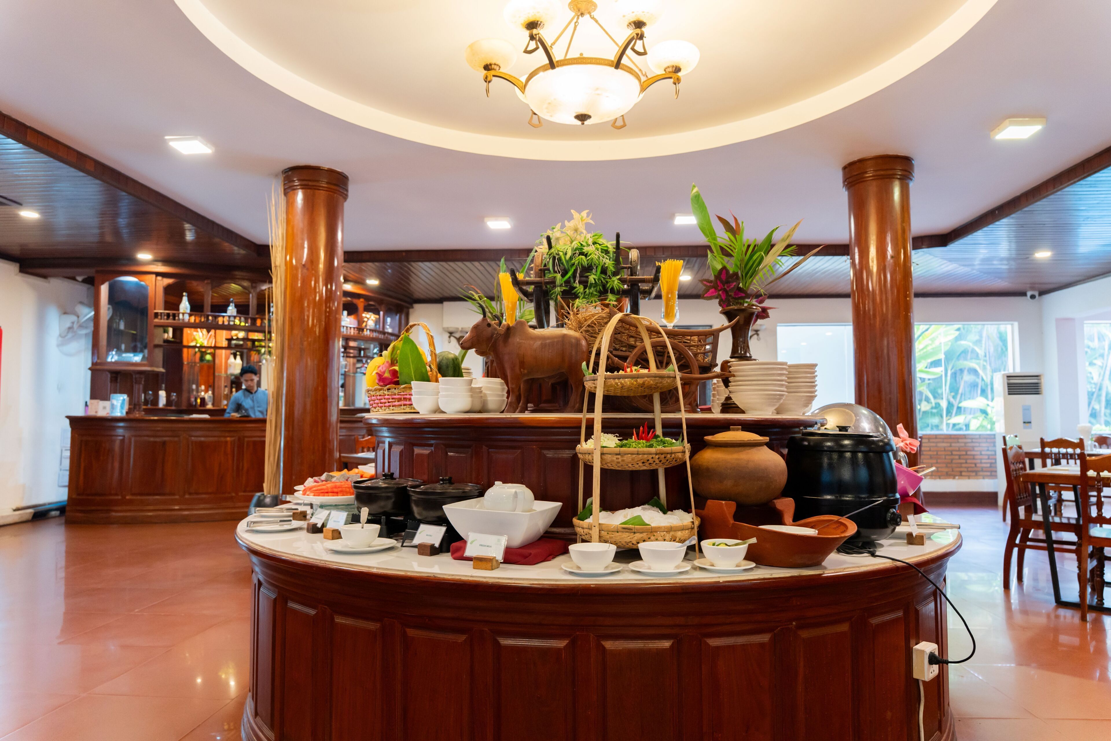 A buffet setup with various dishes, a chandelier, and a bar area in the background.