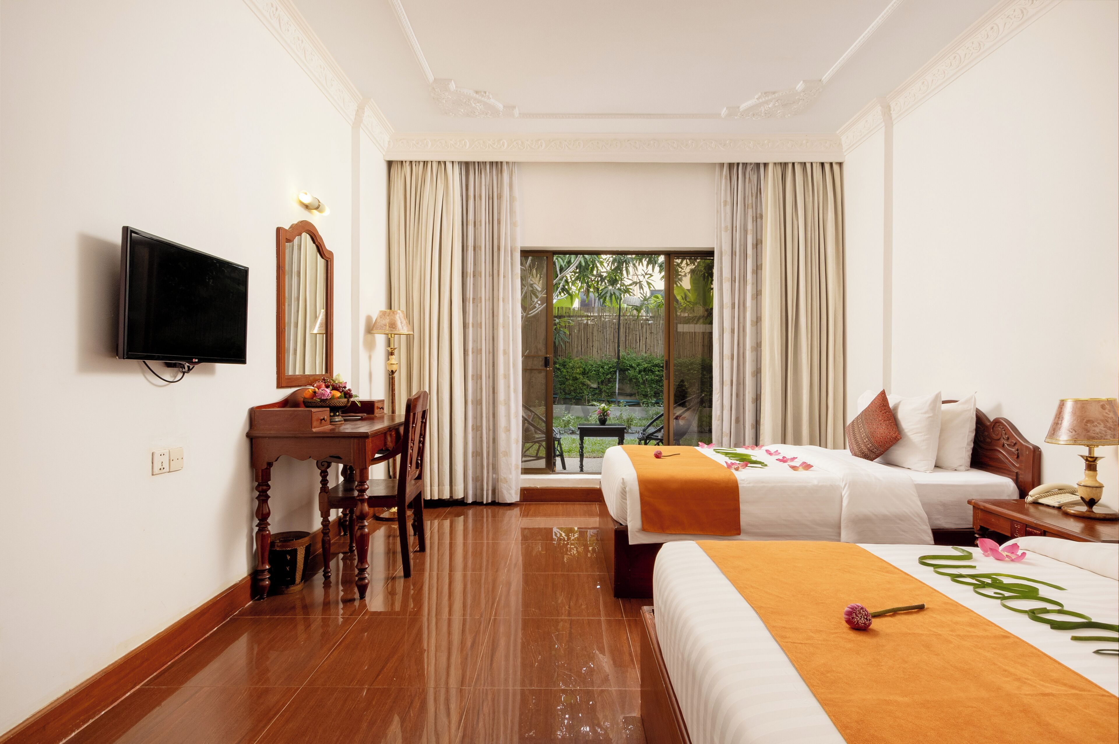 A hotel room with a bed, a desk, a television, and a balcony with curtains.
