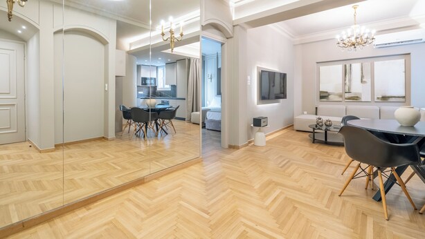 A spacious living area with a wooden parquet floor, a dining table with chairs, a sofa, a TV mounted on the wall, and a chandelier. - Urban Elegance in Kolonaki 7min walk to Syntagma (Athina)