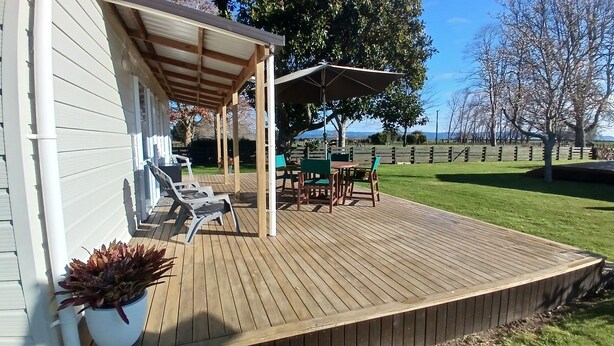 Eine Holzterrasse mit Gartenmöbeln, eine überdachte Veranda und Blick auf eine Rasenfläche.