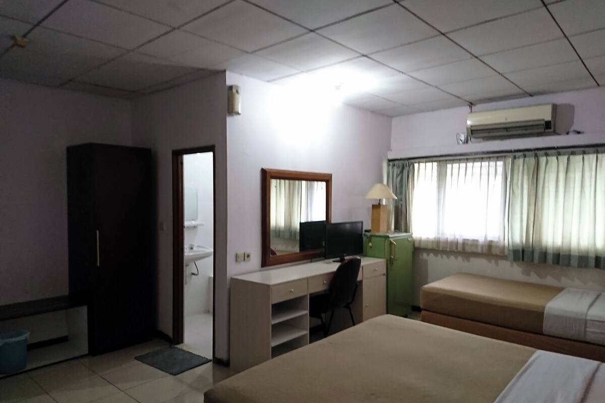 A hotel room with a bed, a desk with a computer, a mirror, a lamp, and an air conditioner.