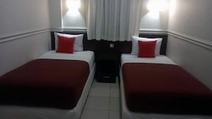 A small hotel room with two single beds, each with a red pillow and white bedding. There are two bedside tables with lamps, and a small window with curtains. - Wisma Shalom  (Jakarta)