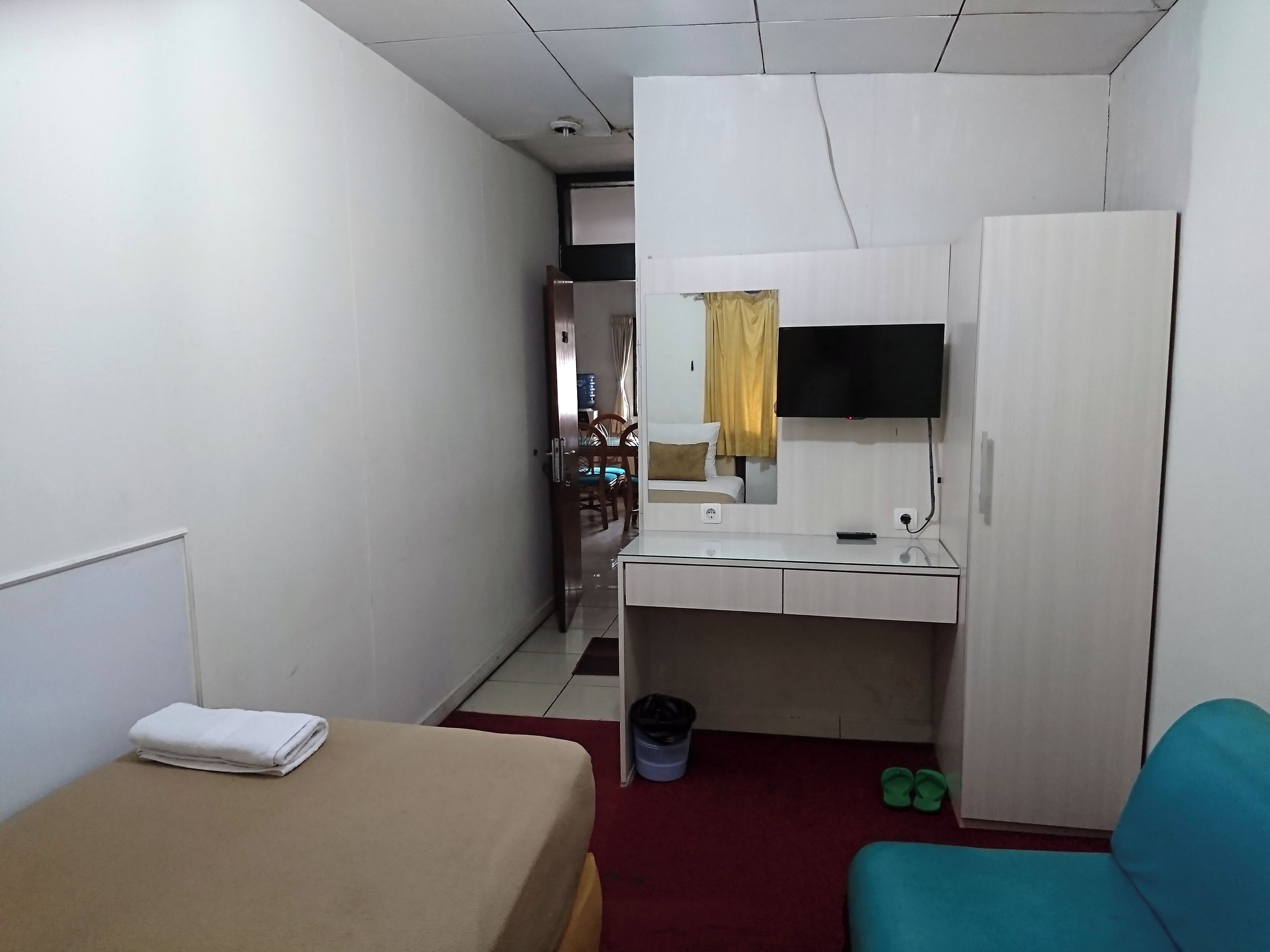 A compact hotel room with a bed, a desk with a mirror, a television, and a wardrobe.
