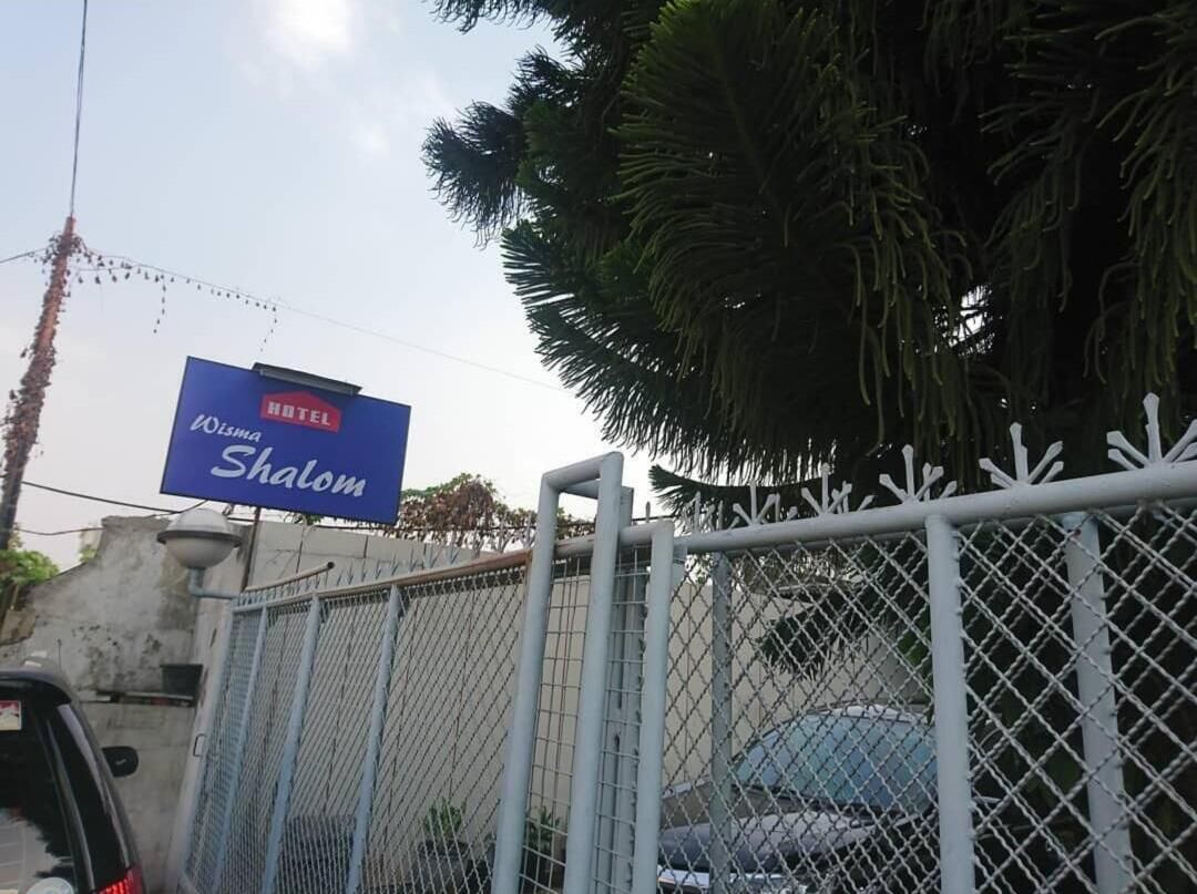 A hotel sign for 'Hotel Wolsha Shalom' with a chain-link fence in the foreground.