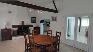 A dining area with a wooden table and chairs, a fireplace, and a kitchen in the background.