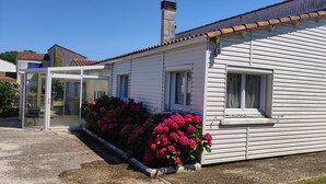 A single-story house with a white exterior, a chimney, and a covered porch with pink flowers.