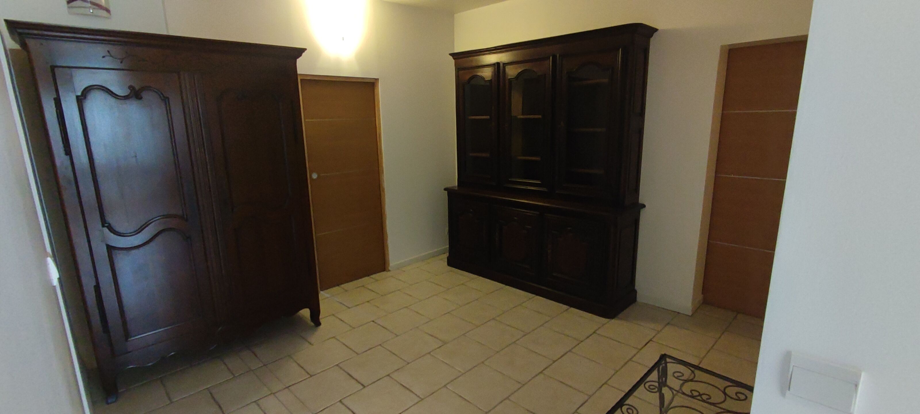 A hallway with two wooden wardrobes, a tiled floor, and a light fixture on the wall.