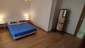 A bedroom with a bed, two bedside tables with lamps, a mirror, and wooden flooring.