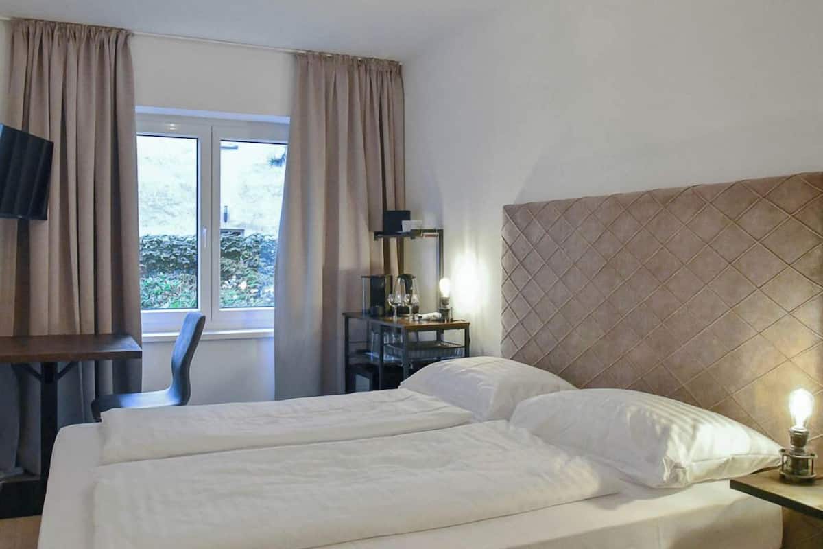 A hotel room with a bed, a desk, a chair, a TV, and a window with curtains.
