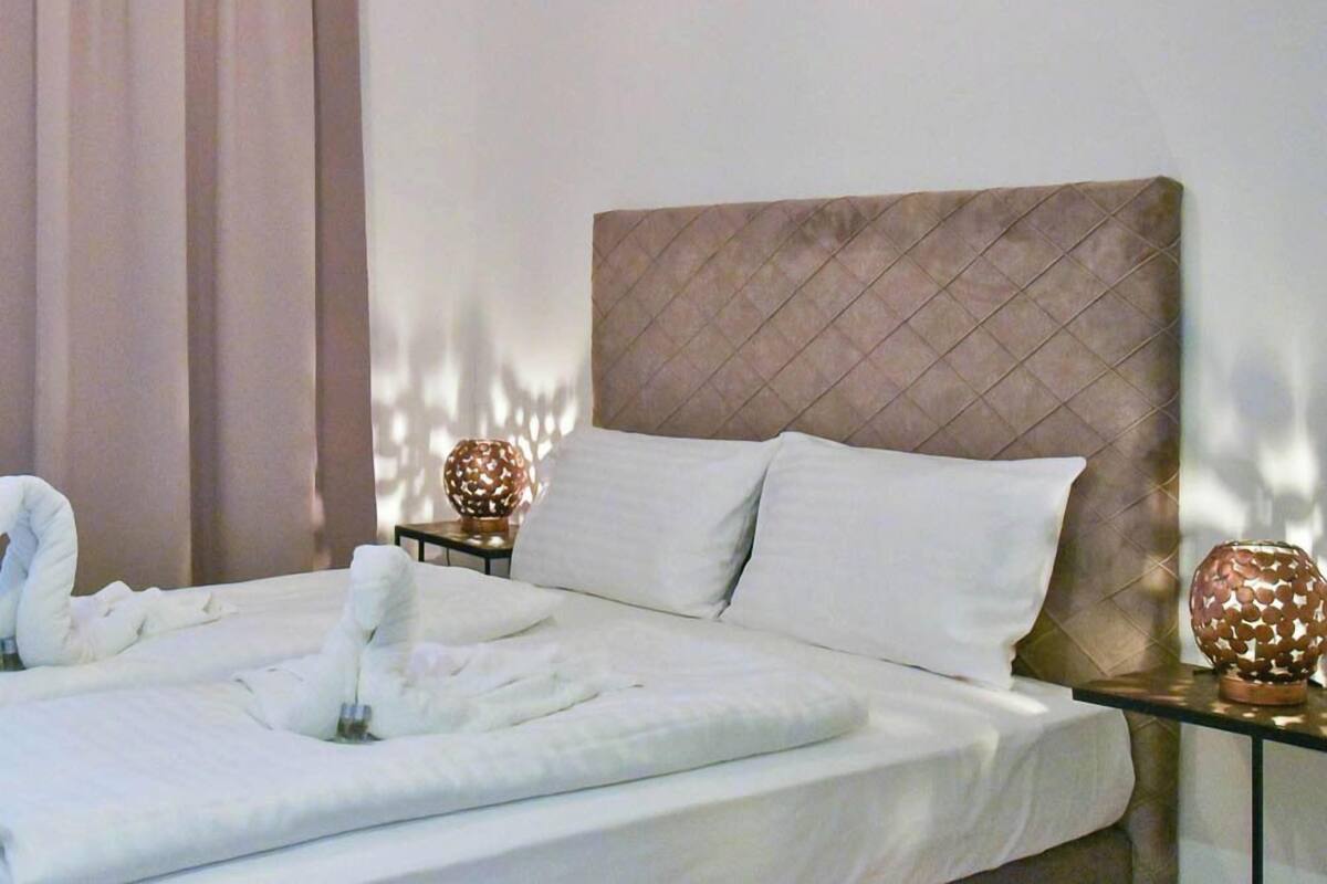 A neatly made bed with white linens and towels, a tufted headboard, and two decorative spherical lamps on nightstands.