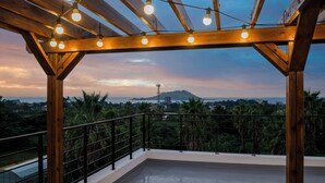 A wooden balcony with a railing, string lights, and a view of the sea and mountains. - Liverpool an spa (Jeju City)
