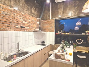 Una cocina con pared de ladrillo, baldosas blancas, campana de acero inoxidable, ventana decorada y encimera de madera.