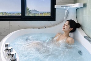 A woman in a bathtub with a view of a mountain and sea through a window. - Liverpool an spa (Jeju City)
