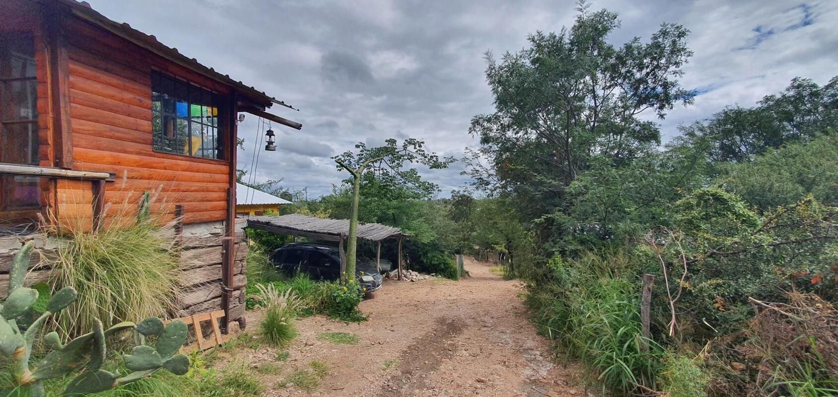 A rustic wooden cabin with a dirt path leading to a covered area.