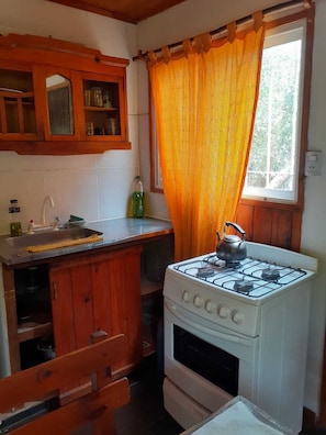 A kitchen with wooden cabinets, a gas stove, a window with orange curtains, and a sink.
