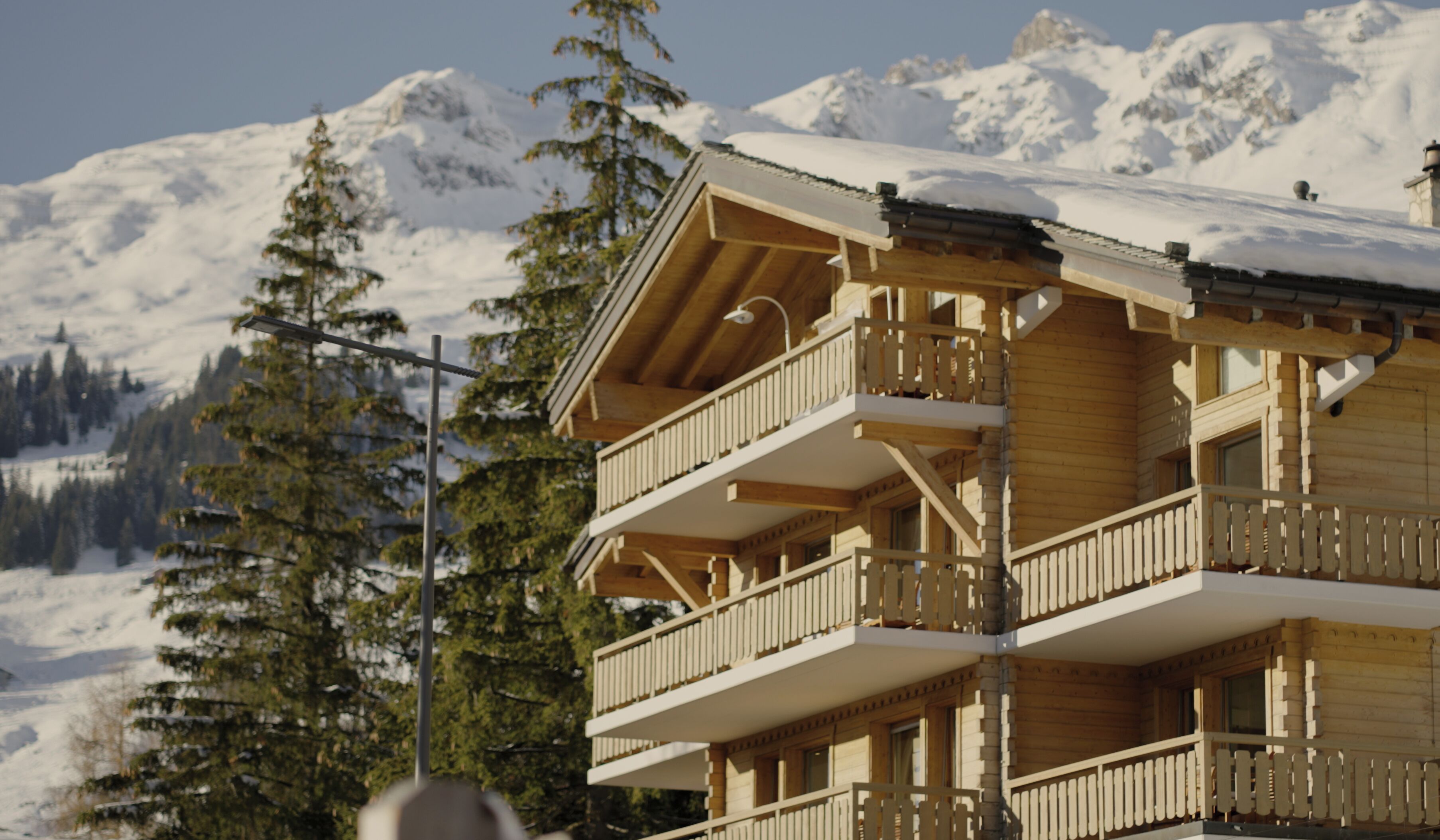 Una cabaña de madera con varios balcones, con una imponente montaña nevada de fondo.