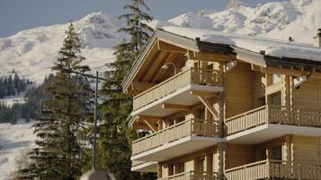 Una cabaña de madera con varios balcones, con una imponente montaña nevada de fondo.