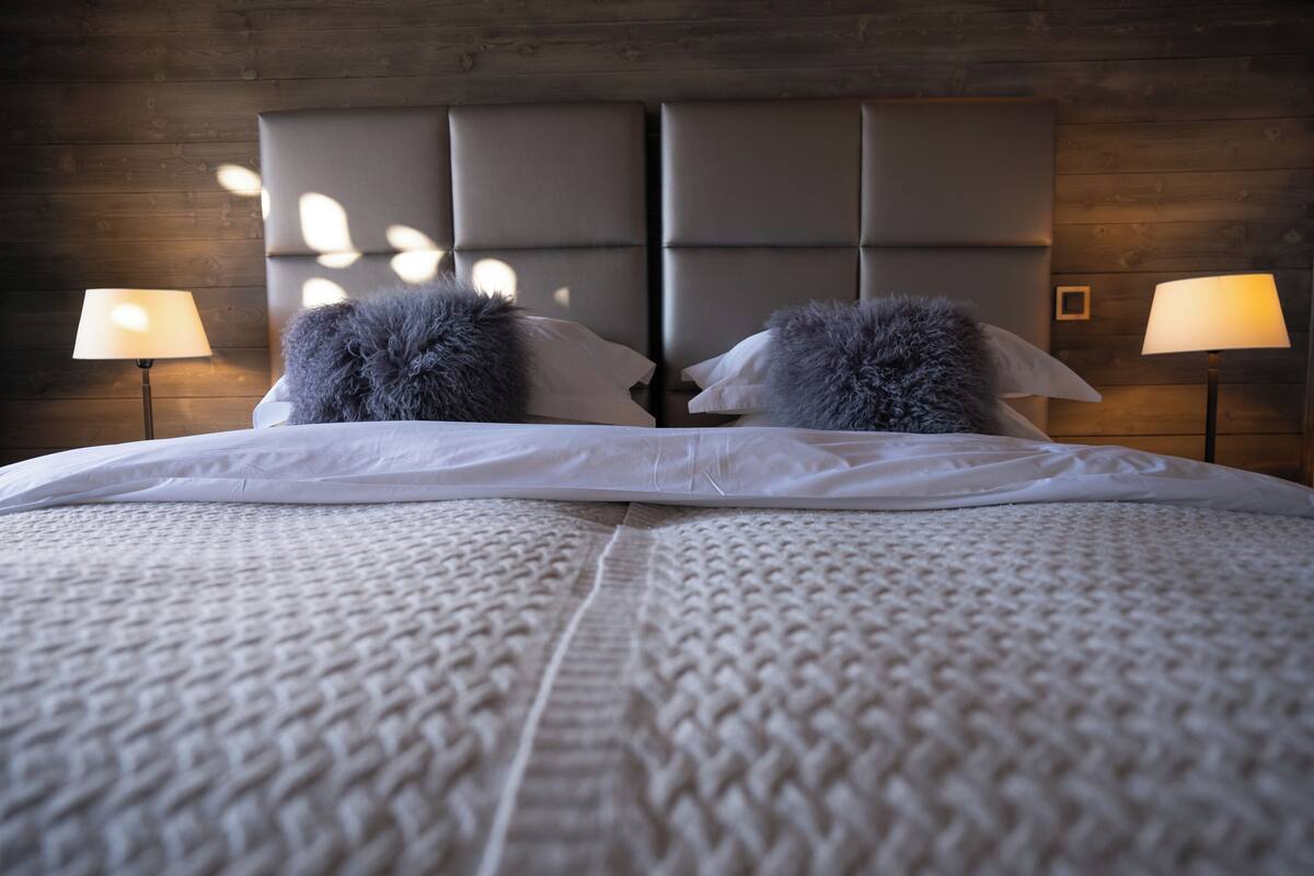 A bed with a tufted headboard, two pillows, and a textured blanket.