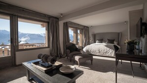 A spacious bedroom with a large bed, a desk, and a view of mountains through large windows. - No.14 Verbier (Bagnes)