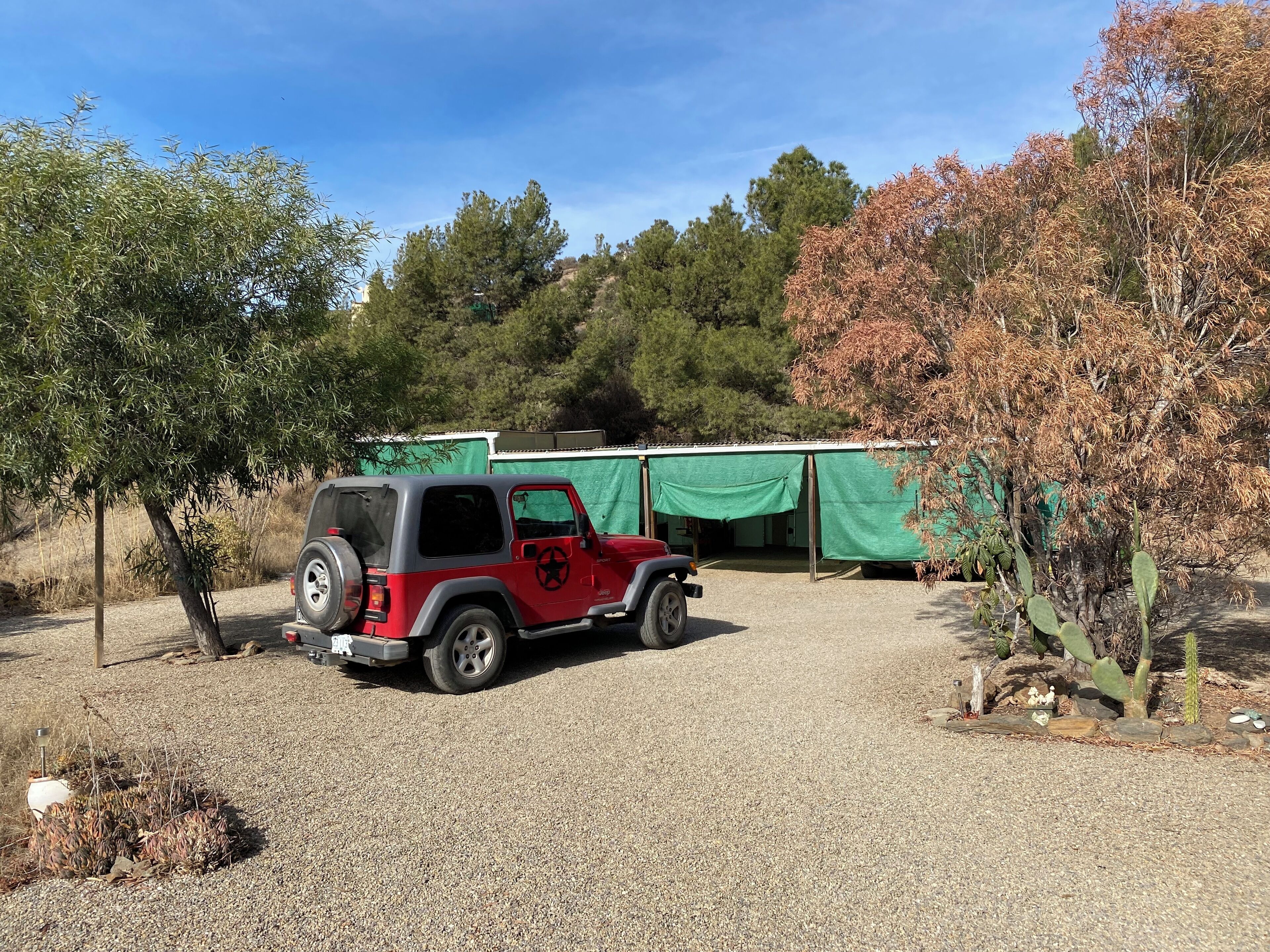 Un jeep rojo estacionado en un área de grava con una estructura de carpa verde al fondo.