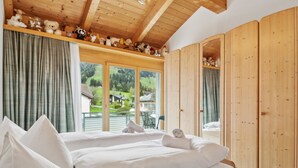A bedroom with a wooden bed, a view of a green landscape, and a collection of stuffed animals on a shelf. - Casa Hermi by Interhome (Churwalden)