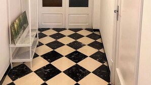 A hallway with a checkered floor, a white door with frosted glass panels, and a metal shelf unit with a painting. - Cozy 2-bedroom apartment with WiFi, air-con and a  rooftop terrace with bbq. (LLUCMAJOR)