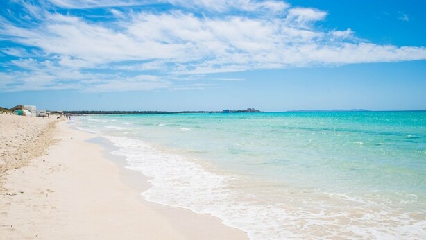 A beach with clear turquoise water, a sandy shore, and a few distant buildings. - Cozy 2-bedroom apartment with WiFi, air-con and a  rooftop terrace with bbq. (LLUCMAJOR)
