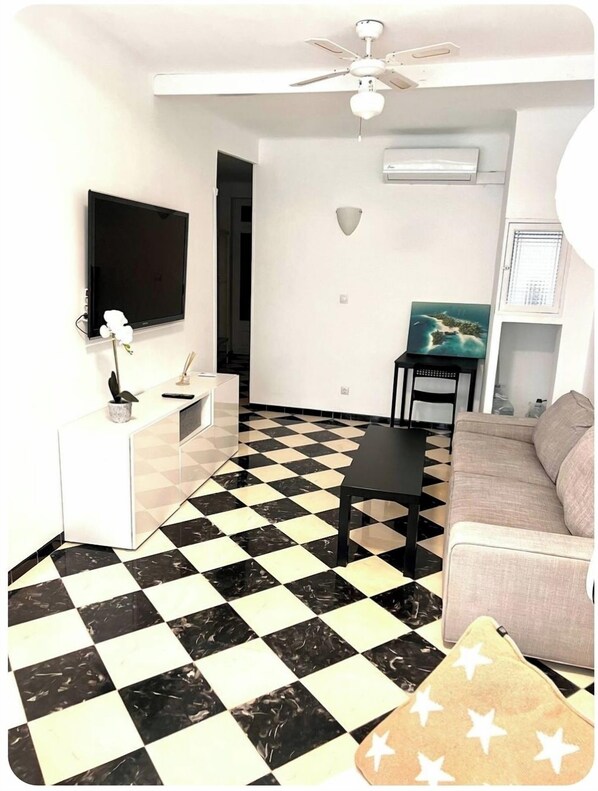 A living room with a black and white checkered floor, a flat-screen TV mounted on the wall, a ceiling fan, and a sofa.