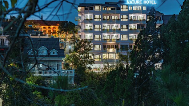Un hôtel à plusieurs étages, avec une enseigne indiquant « Hôtel Nature », des balcons ornés de plantes et une vue sur les bâtiments environnants.