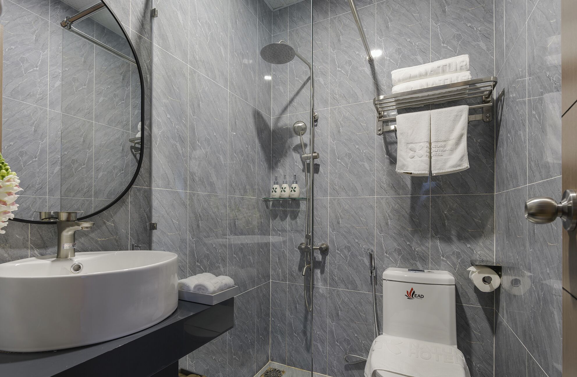 Une salle de bain moderne avec un lavabo rond, une cabine de douche en verre, des toilettes et un porte-serviettes sur lequel est pliée une serviette.
