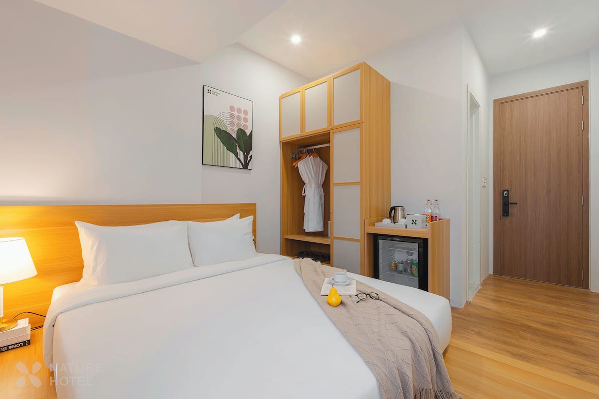 A hotel room with a neatly made bed, a wardrobe, a small desk with a lamp, and a door.