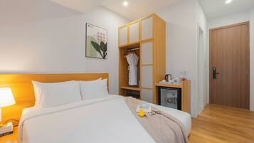 Una habitación de hotel con una cama bien hecha, un armario, un escritorio pequeño con una lámpara y una puerta.