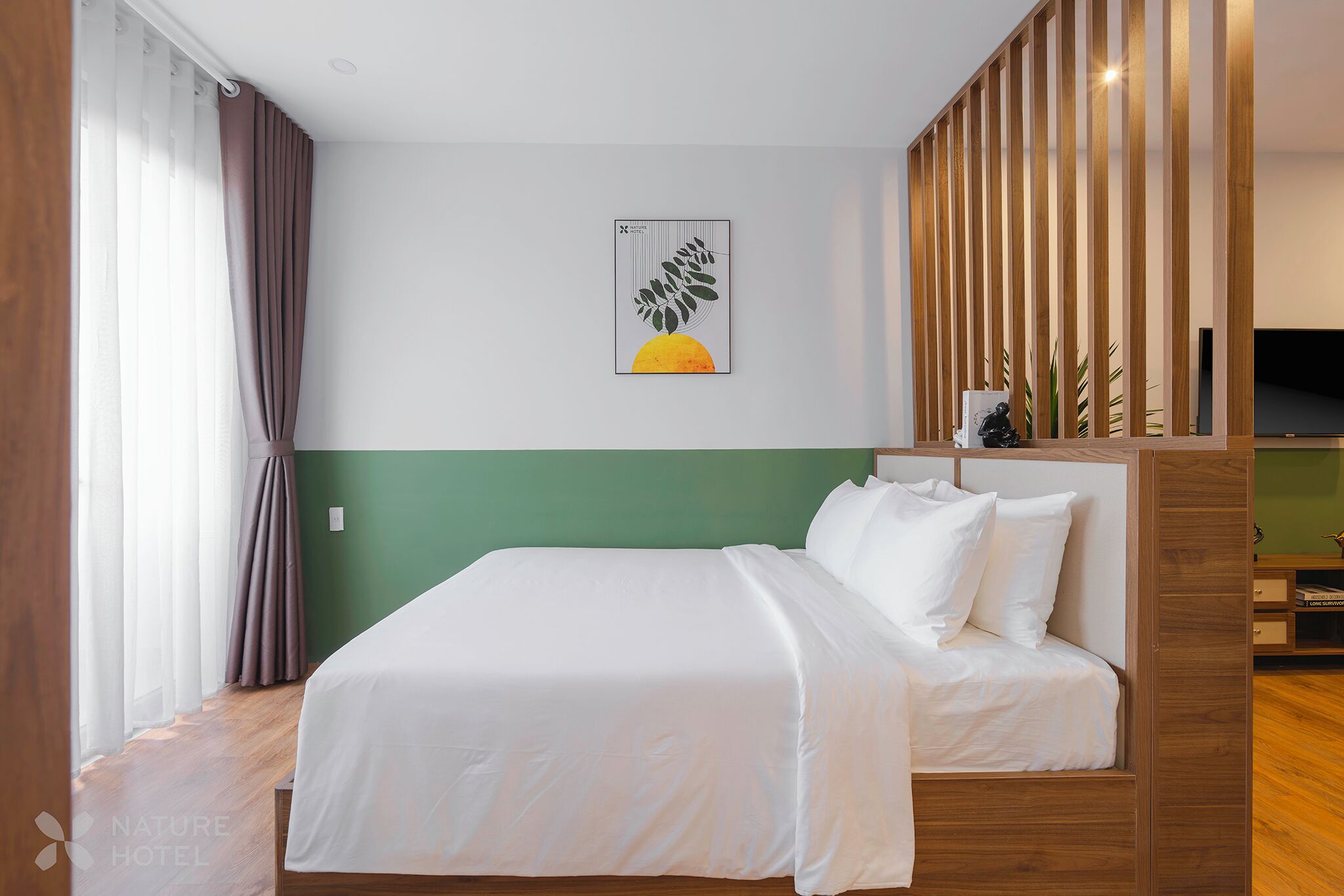 A hotel room with a bed, a green accent wall, a wooden partition, and a framed artwork.