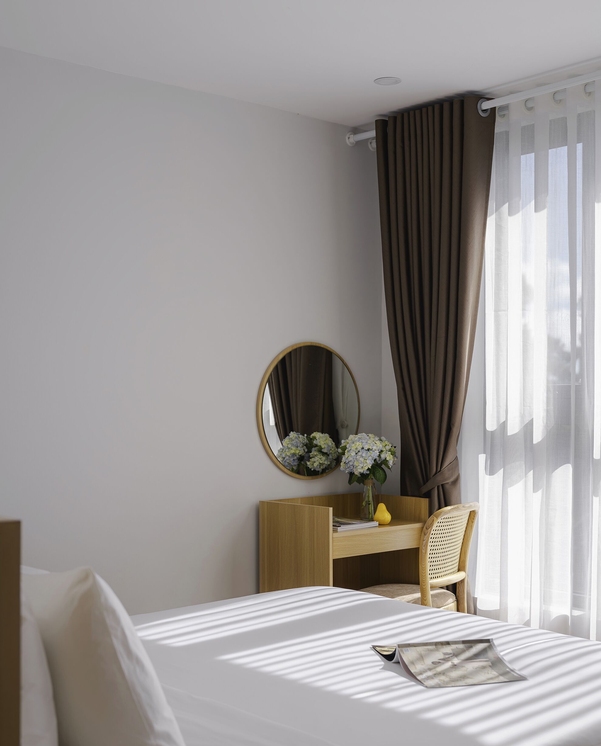 A hotel room with a bed, a desk with a chair, a mirror, and a window with curtains.
