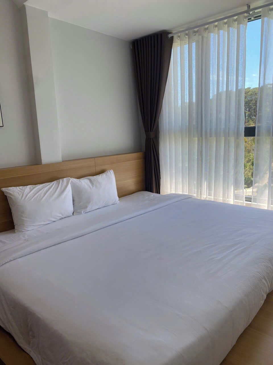 Una cama grande con sábanas blancas, cabecera de madera y cortinas de encaje.