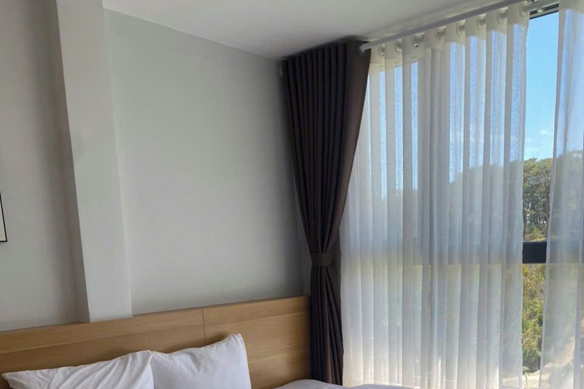 A large bed with white linens, a wooden headboard, and sheer curtains.