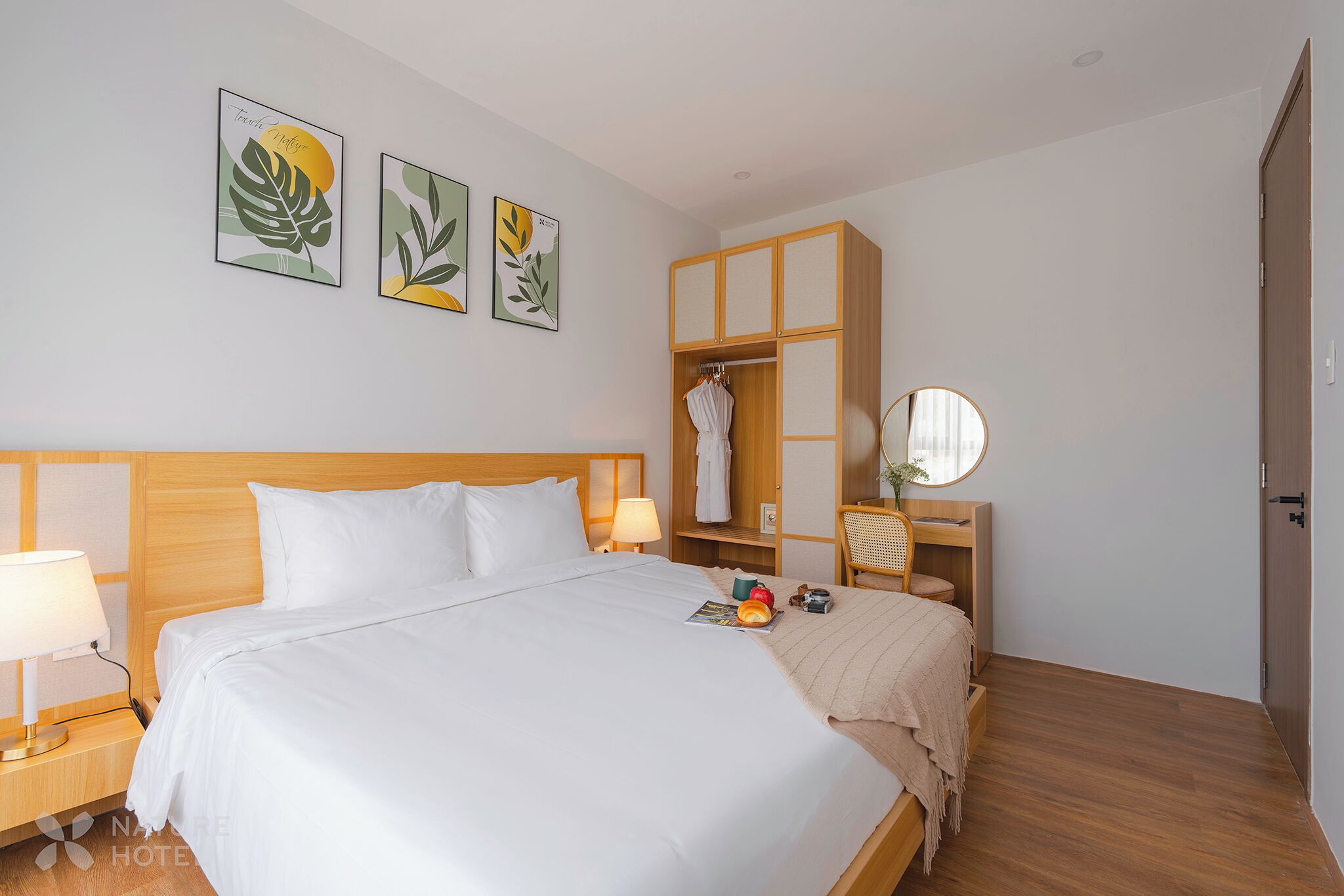 A hotel room with a large bed, wooden headboard, a wardrobe, a bedside table with a lamp, and artwork on the wall.