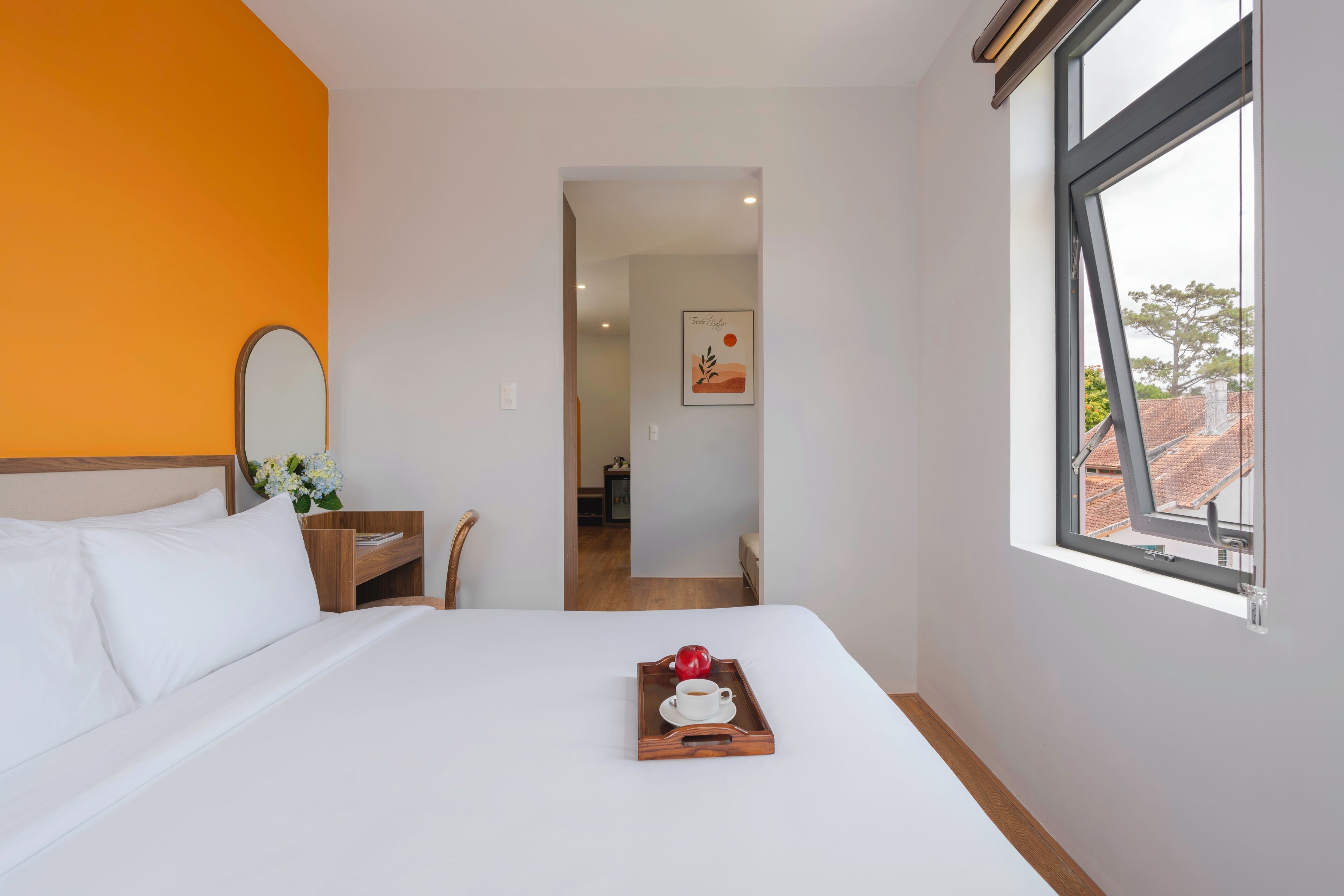 Habitación de hotel con cama, ventana, mesita de noche de madera y bandeja con taza y manzana.