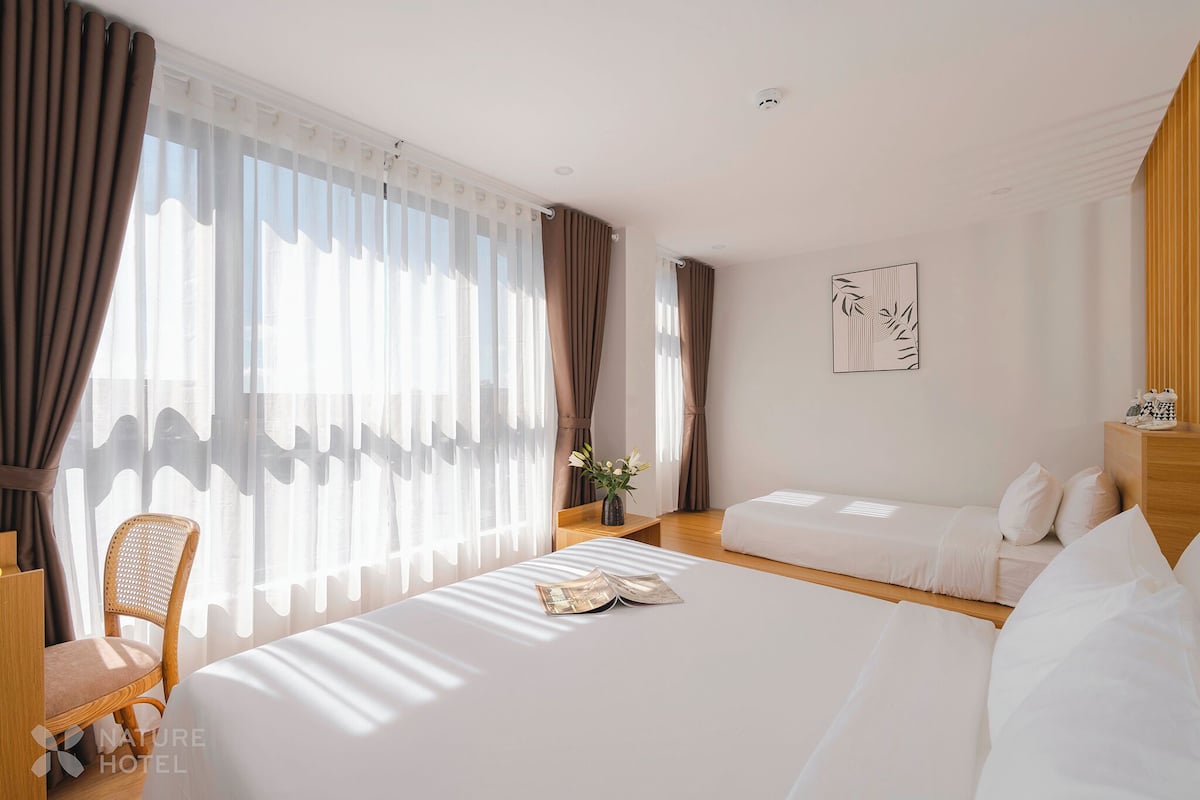 A hotel room with a large bed, a chair, a small table with a vase, and a sofa.
