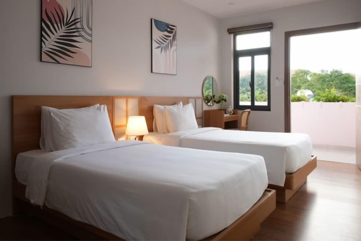 A hotel room with two beds, a window, and artwork on the walls.