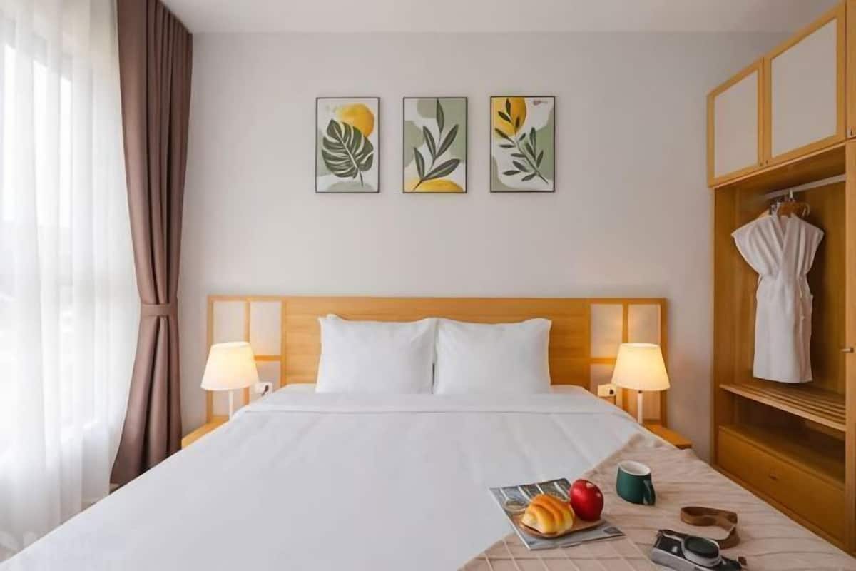 A hotel room with a bed, two bedside lamps, a wooden headboard, a nightstand, a magazine, a cup, and a robe hanging on a wooden rack.