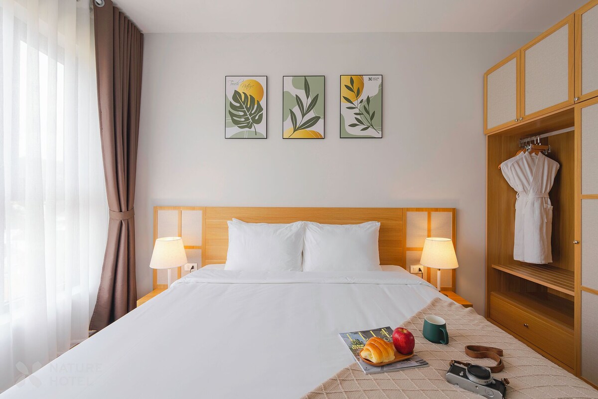 A hotel room with a bed, two bedside lamps, a wooden wardrobe, and three framed artworks on the wall.