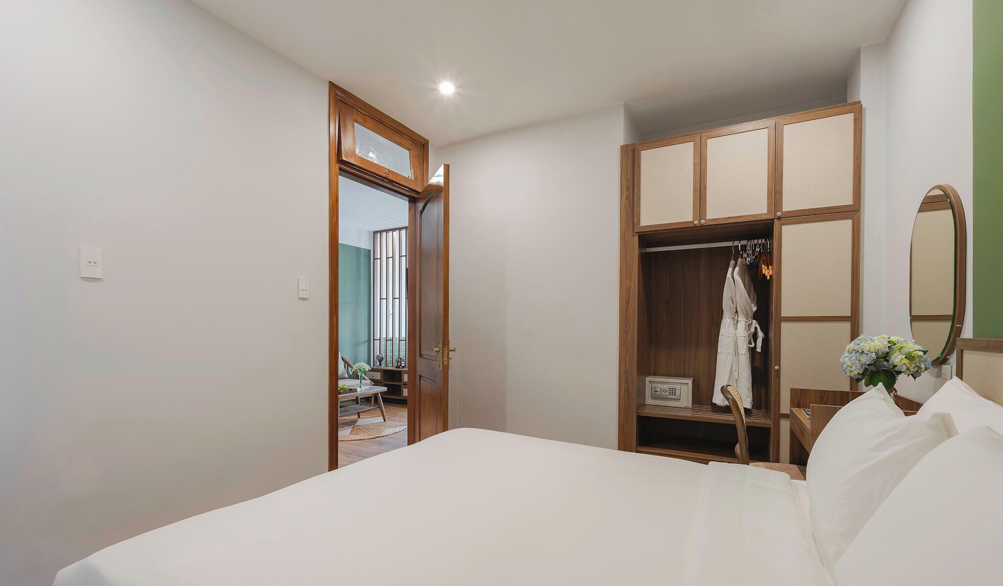 A bedroom with a bed, a wooden wardrobe, a mirror, and a door leading to another room.